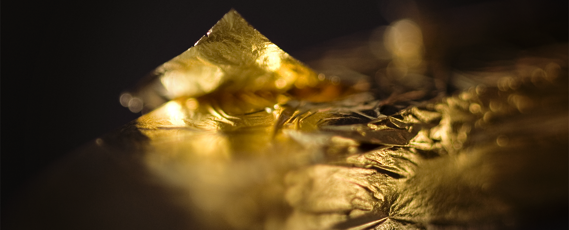 Gros plans d’une feuille d’or aux ton chaud, froissée et scintillante. Sur un fond noir.